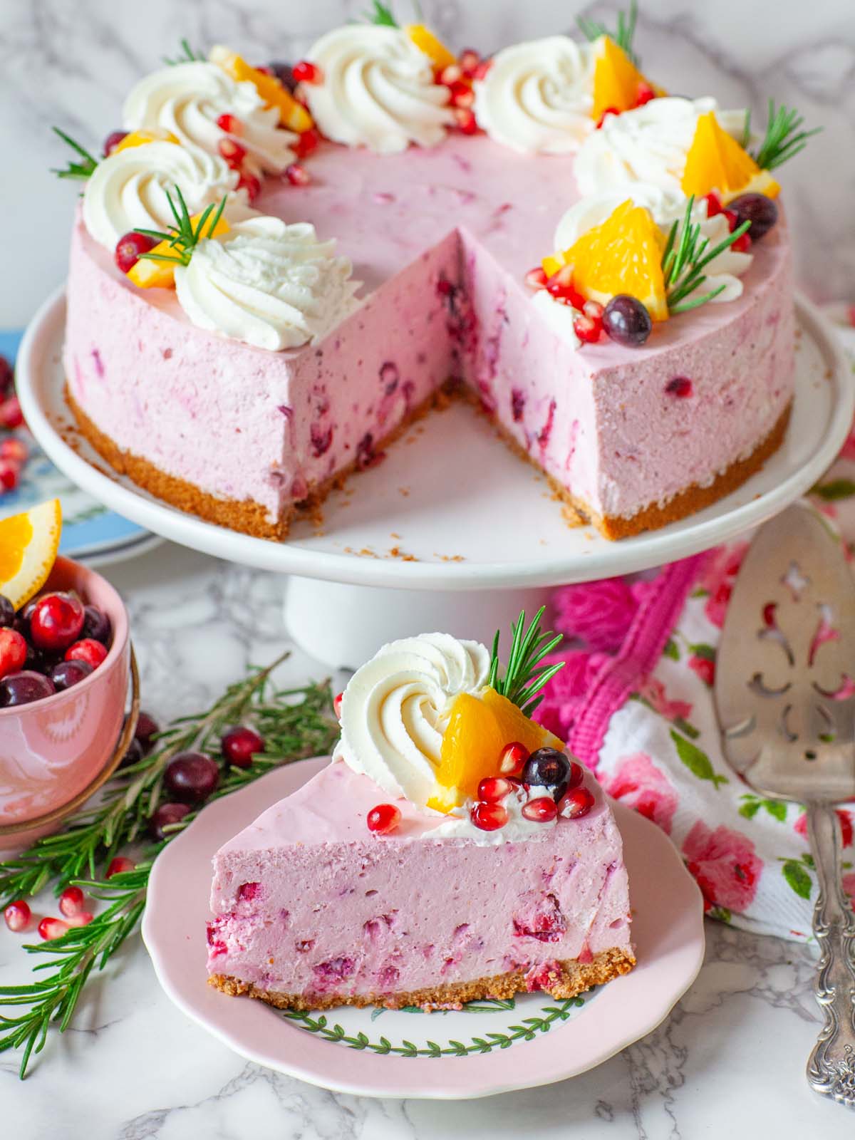 A slice of cheesecake on a plate next to a sliced cheesecake on a cake stand.