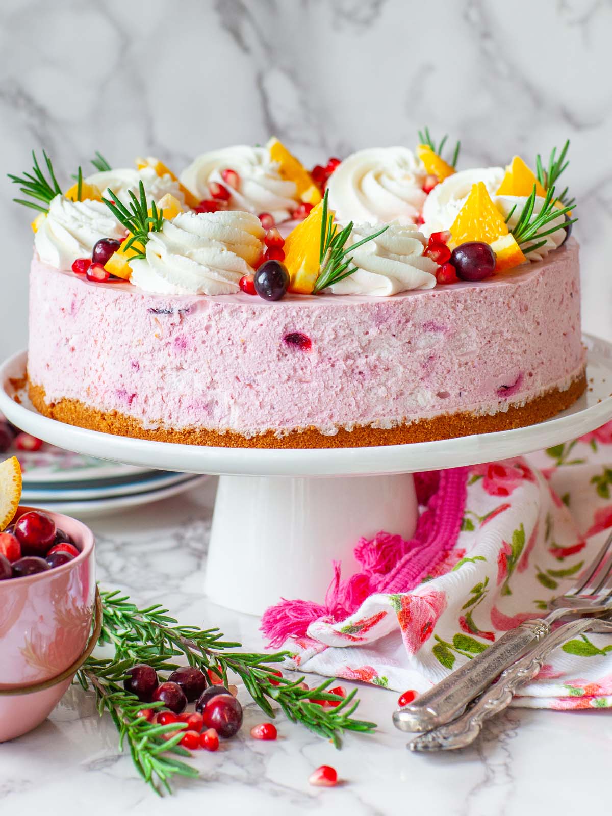 A cheesecake on a cake stand topped with whipped cream and fruit, on a table.