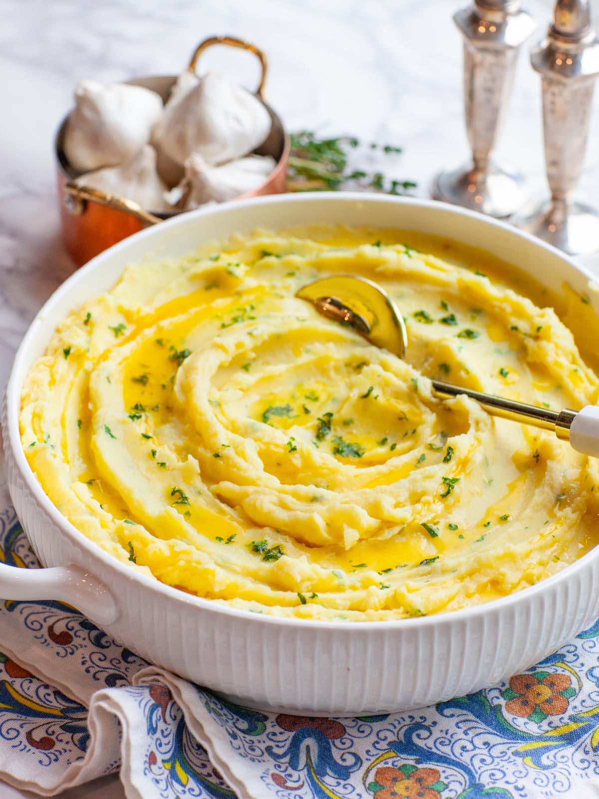 A closeup image of mashed potatoes with herbs in a serving bowl with a spoon.