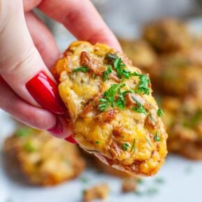A closeup image of a hand holding a cheese mushroom crostini.