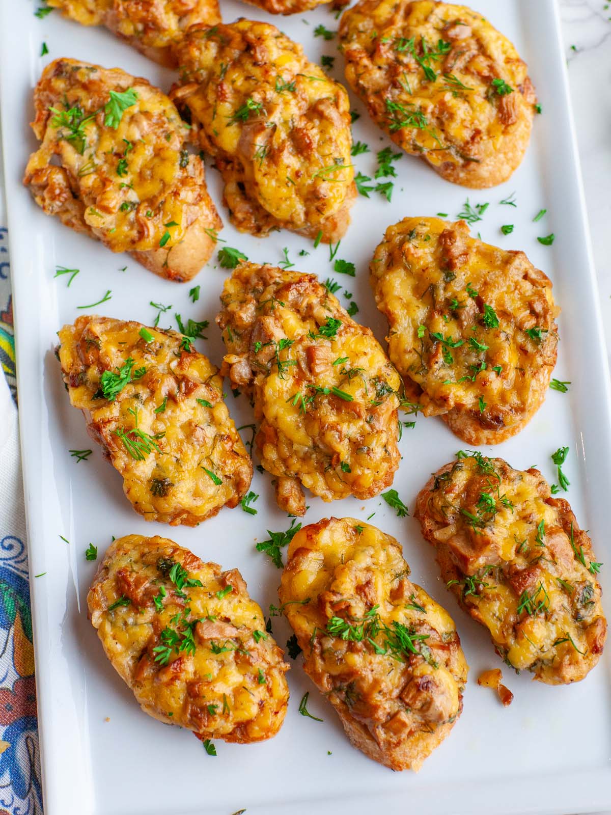 A tray filled with cheesy crostini appetizer, topped with fresh herbs.