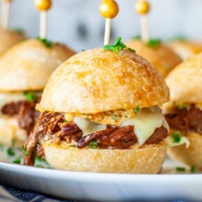 A closeup image of a beef slider sandwich with cheese and spread.