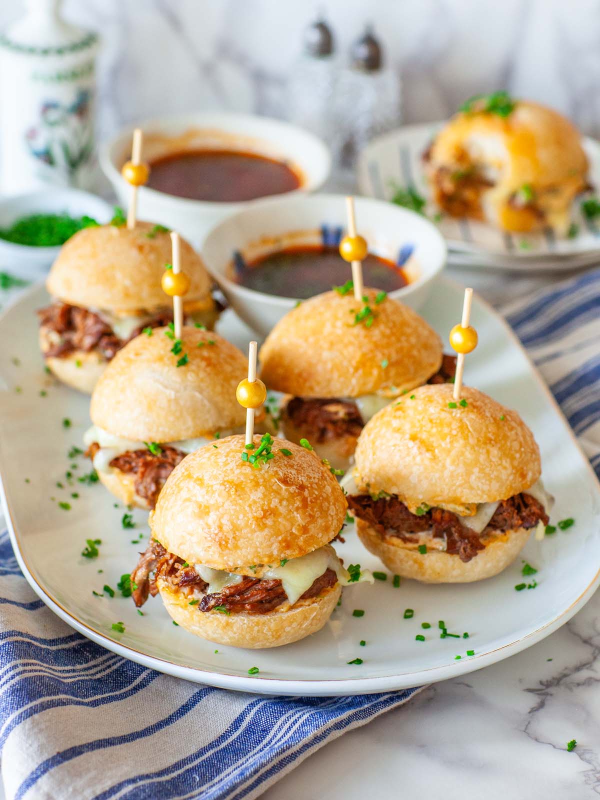 A tray with beef sliders and dipping sauce on a table.