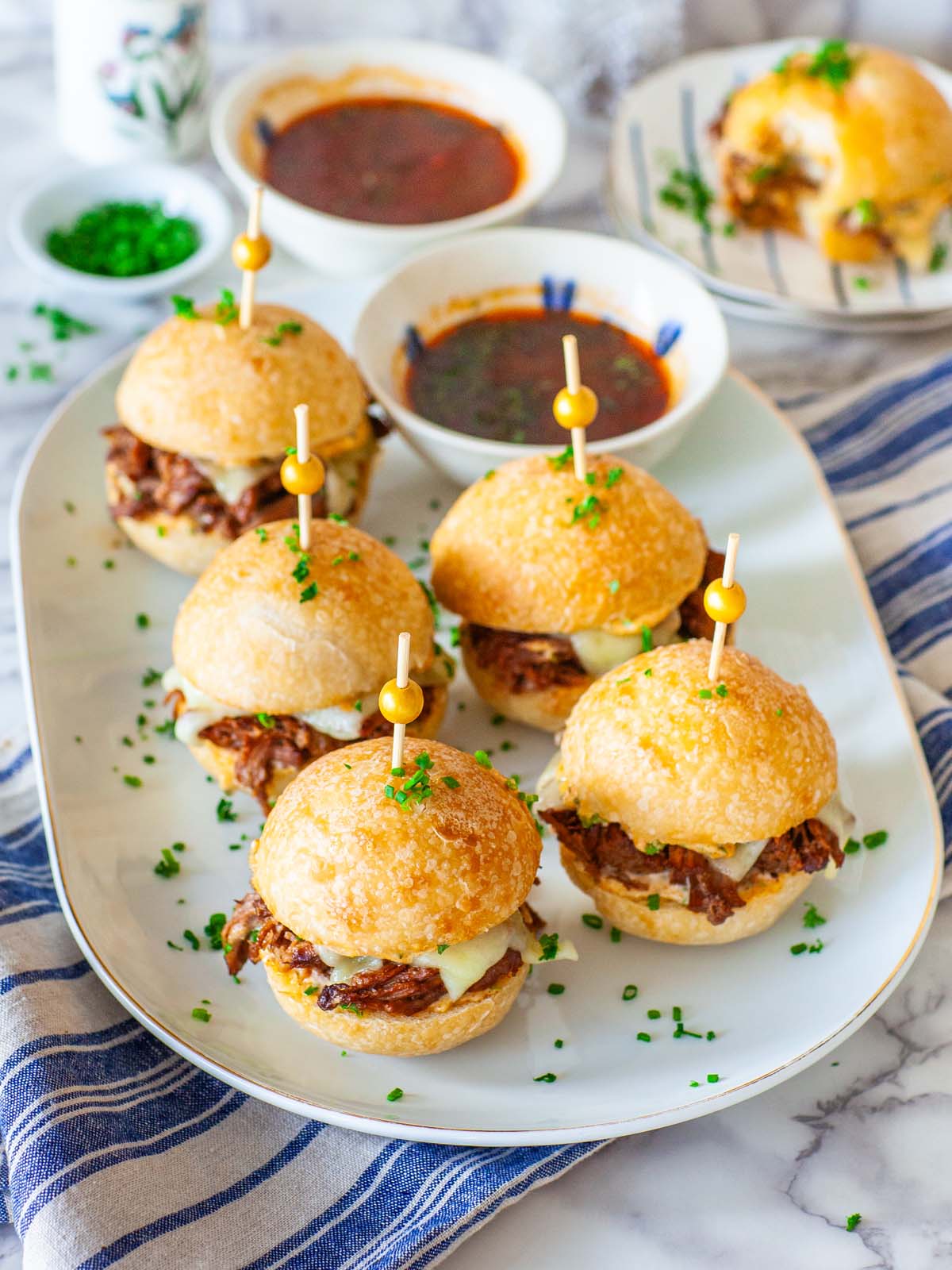 Several beef slider sandwiches on a tray, on a table with dipping sauce.