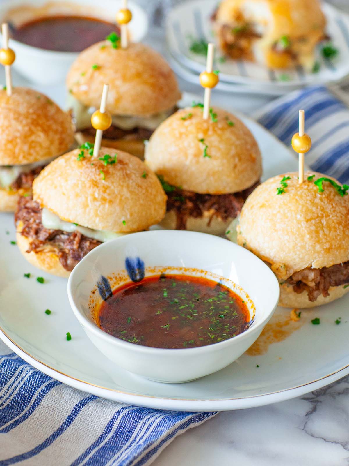 A closeup bowl of sandwich dip on a plate with beef sandwiches.
