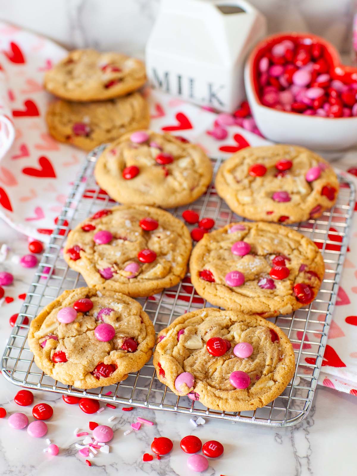 Cookies with M&Ms on a cooling rack, on a table with more cookies.