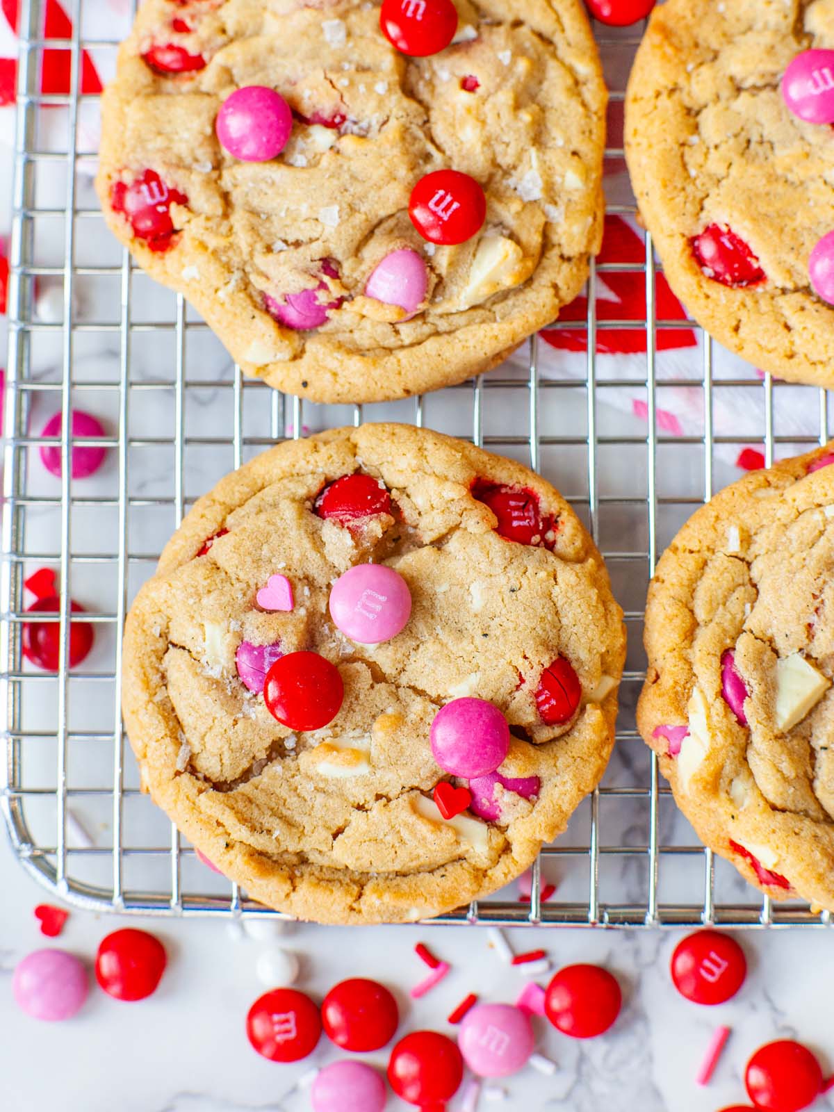 A closeup image of brown butter and chocolate cookies on a wire rack, with pink and red M&Ms.