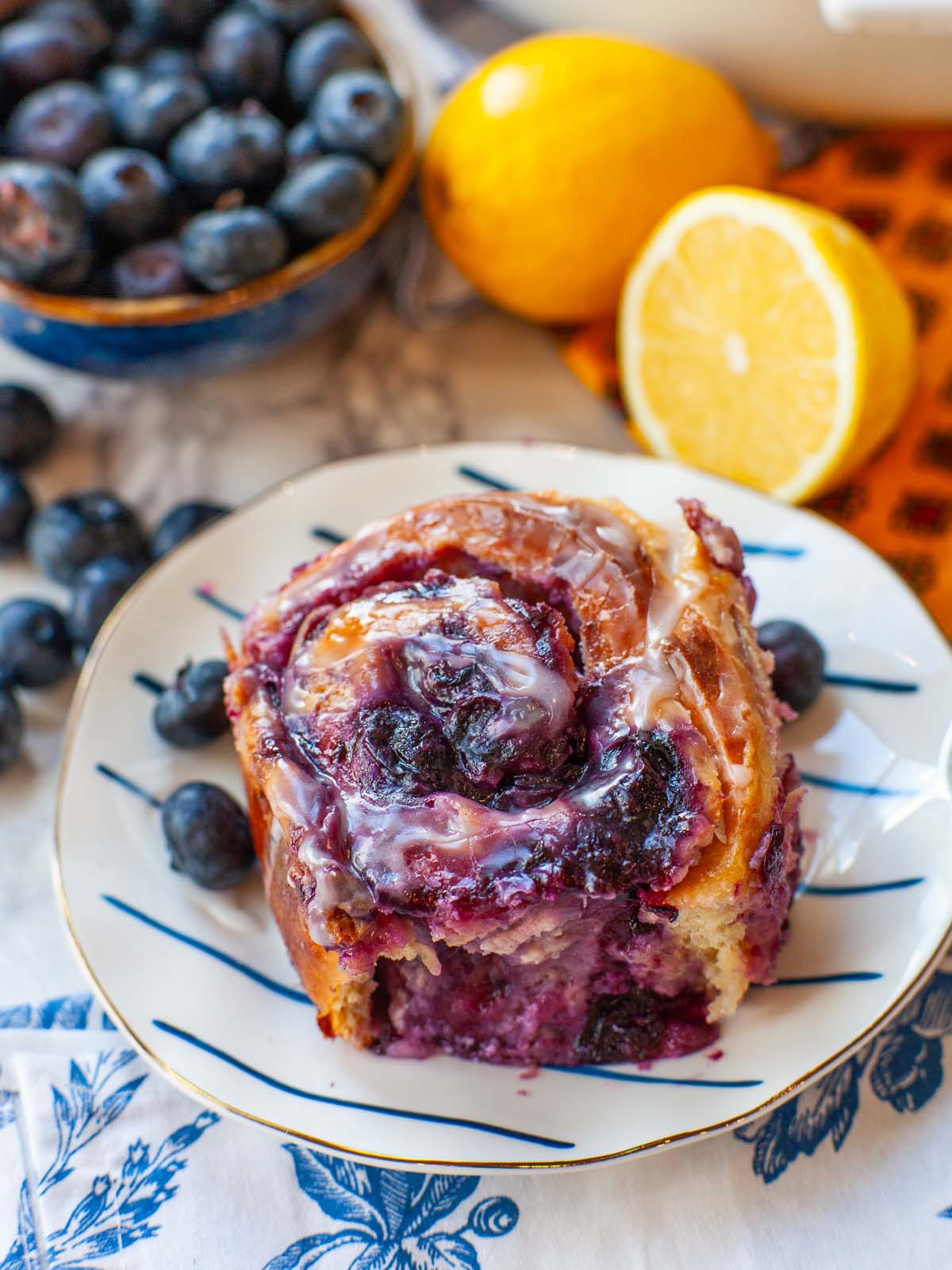 A closeup image of cinnamon roll with blueberries, on a table with lemons and berries.