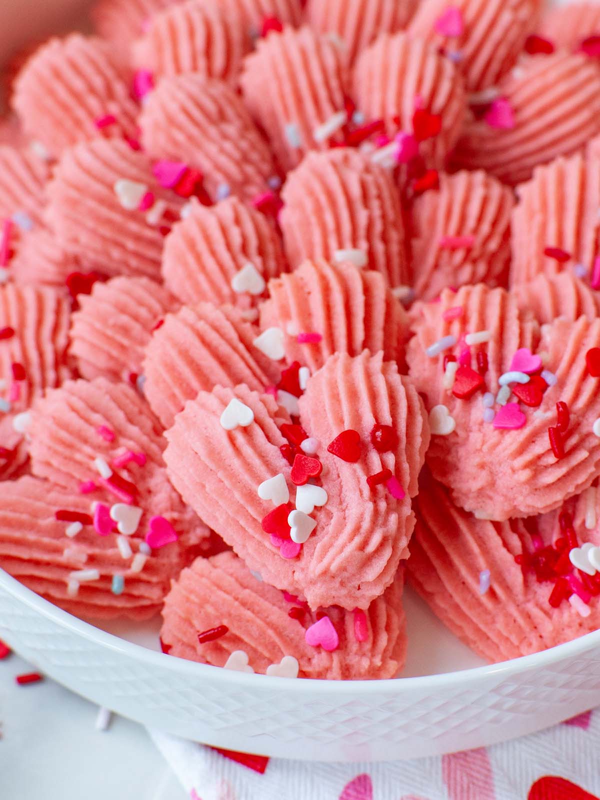 A closeup image of heart-shaped pink cookies with sprinkles.