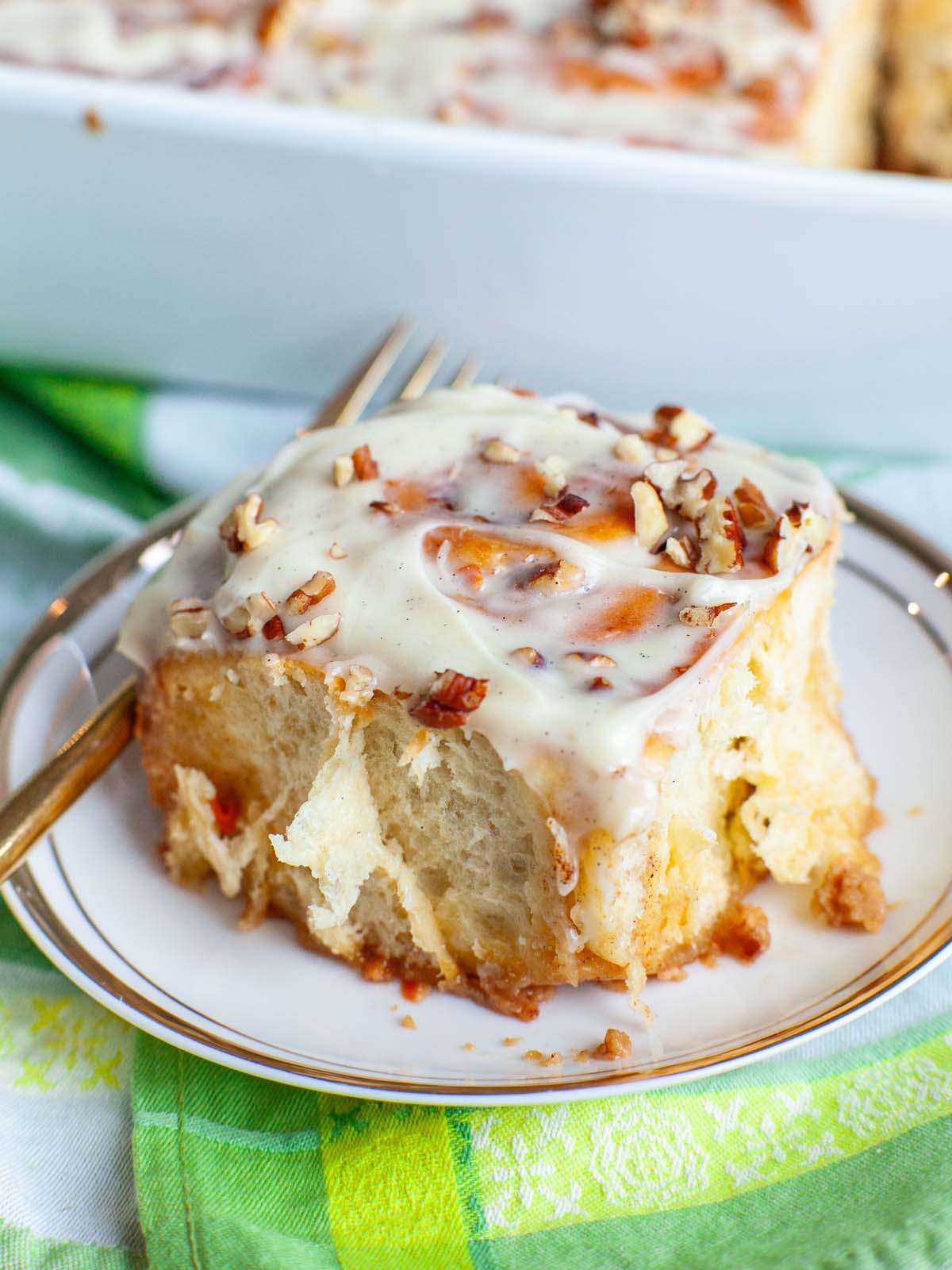 A closeup image of a cinnamon roll on a plate with a fork.