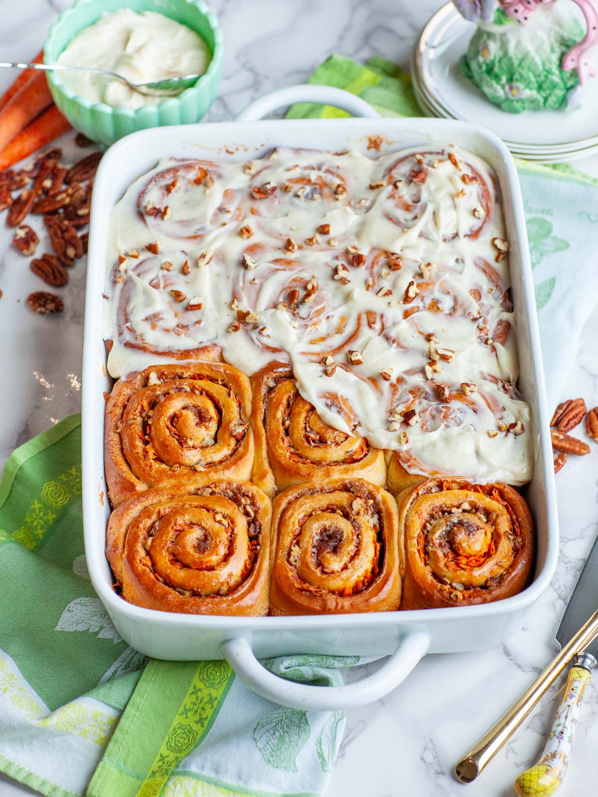 A casserole dish of cinnamon rolls with icing on a table with utensils.