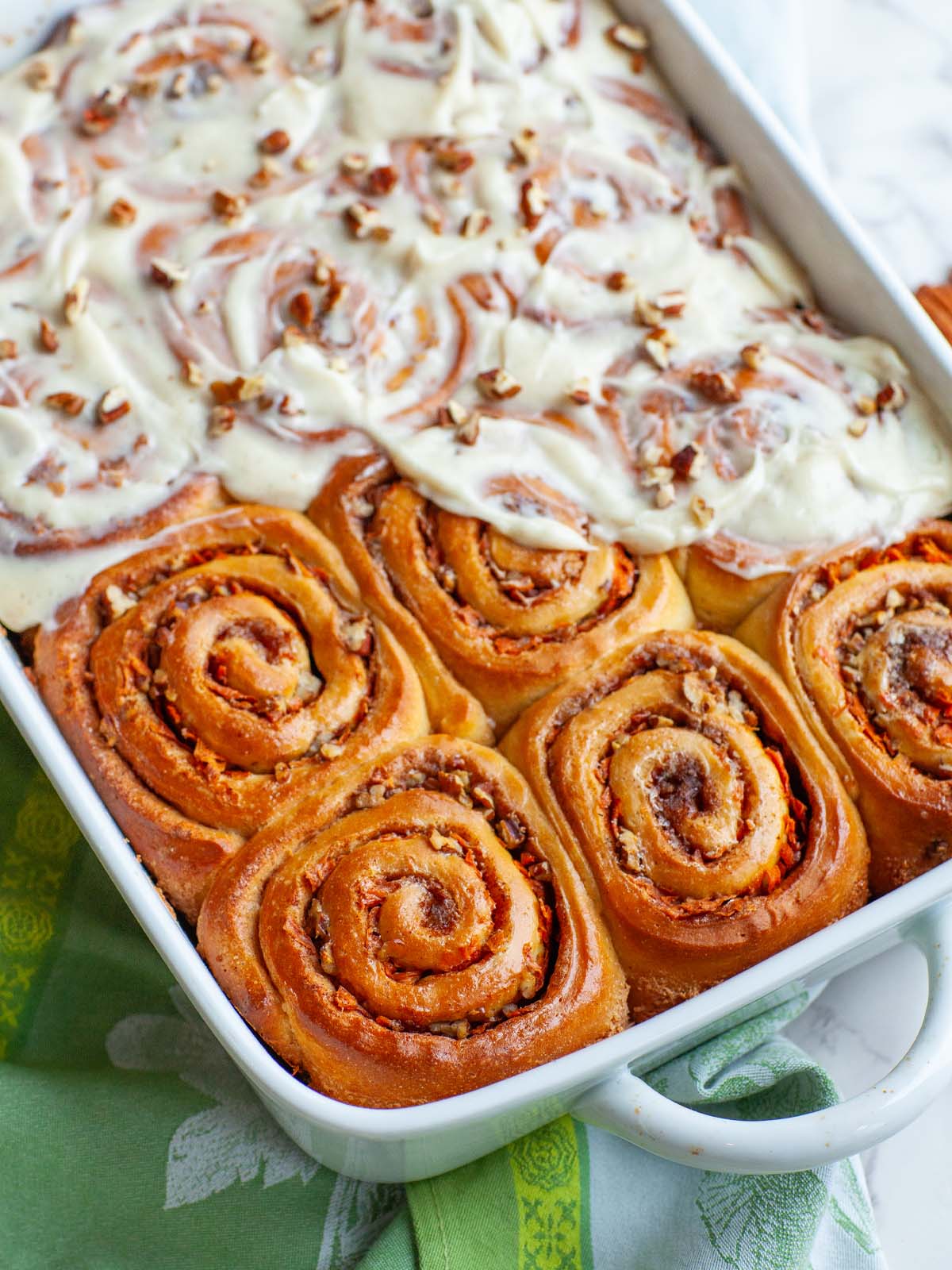 A close up image of carrot cake cinnamon rolls with icing in a casserole dish.