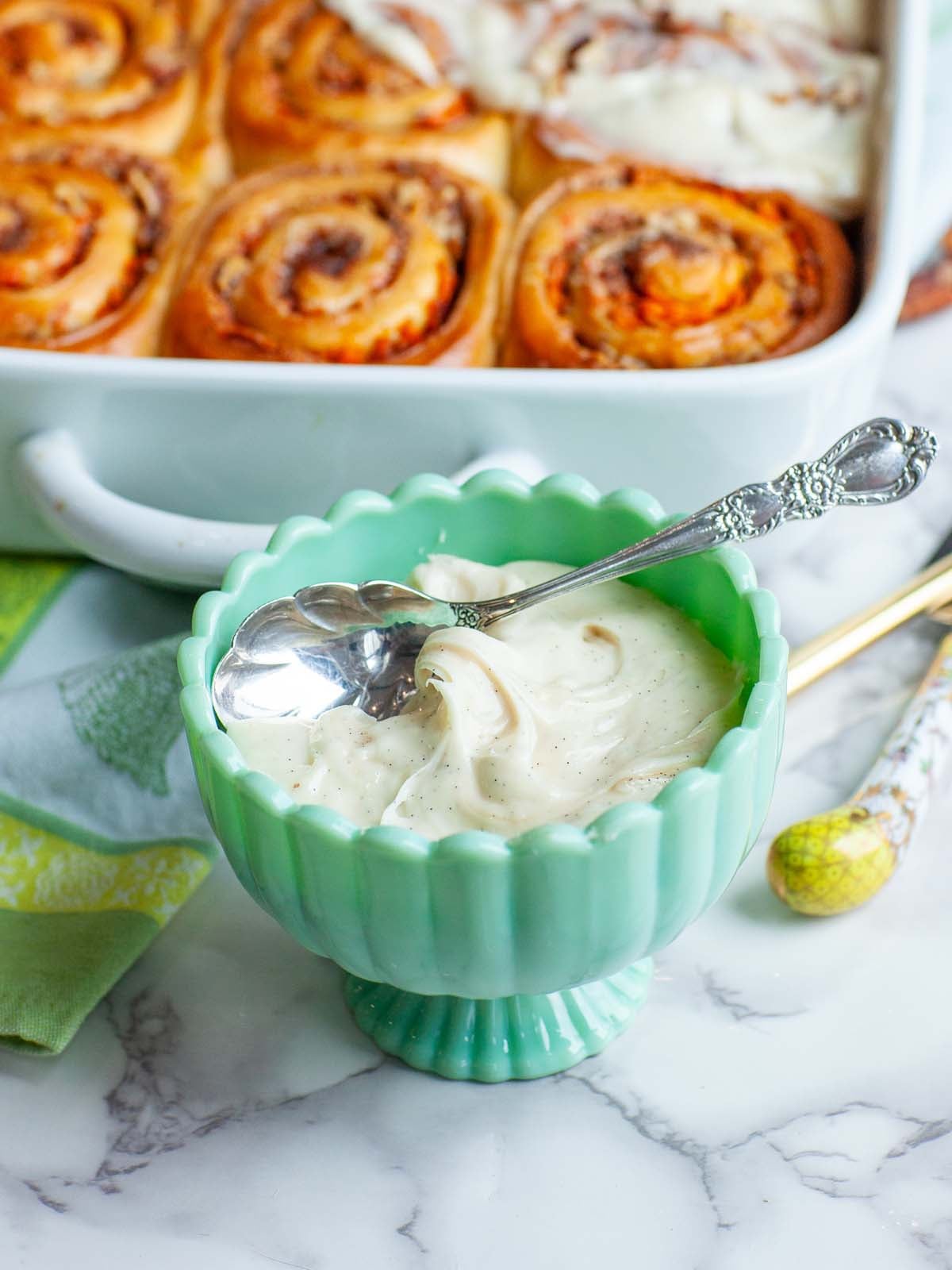A closeup image of cream cheese icing in a small bowl, with a spoon.