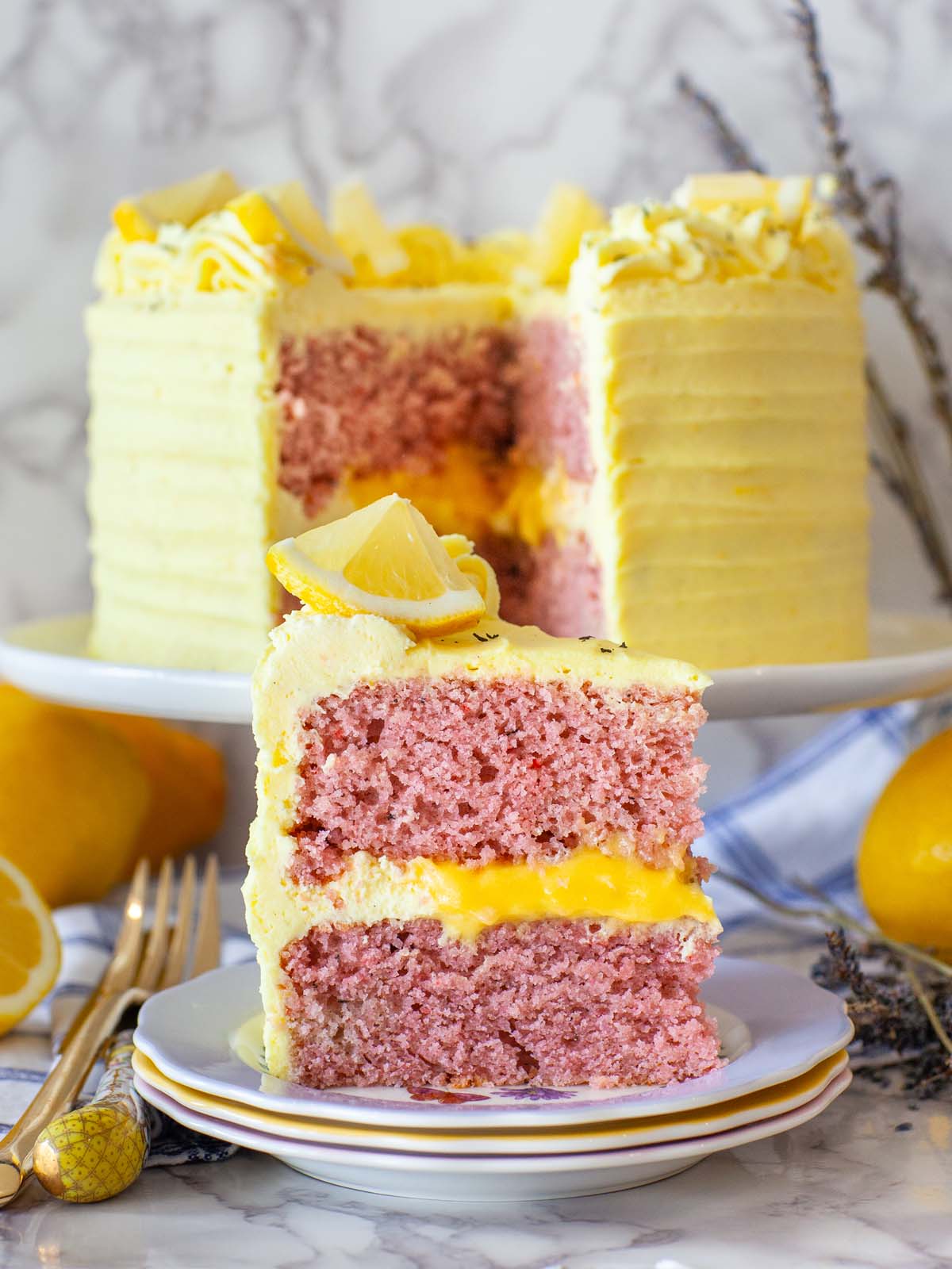 A closeup image of a slice of cake on a plate, with a cake in the background.