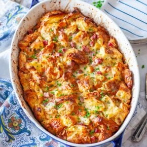 An oval casserole dish with croissant casserole, dotted with ham; on a table with plates and utensils.