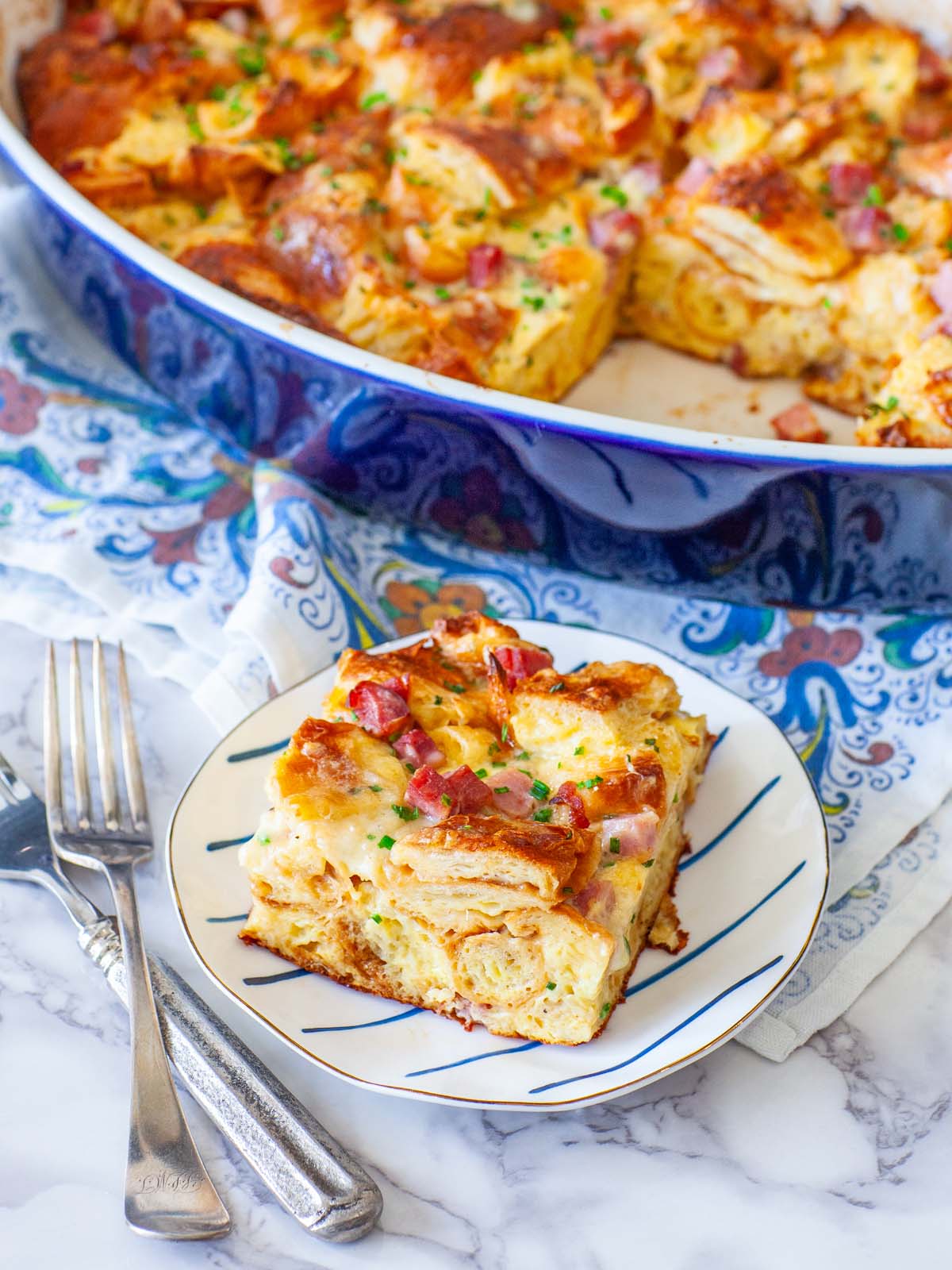 A closeup image of ham croissant casserole on a plate, with a large dish in the background.