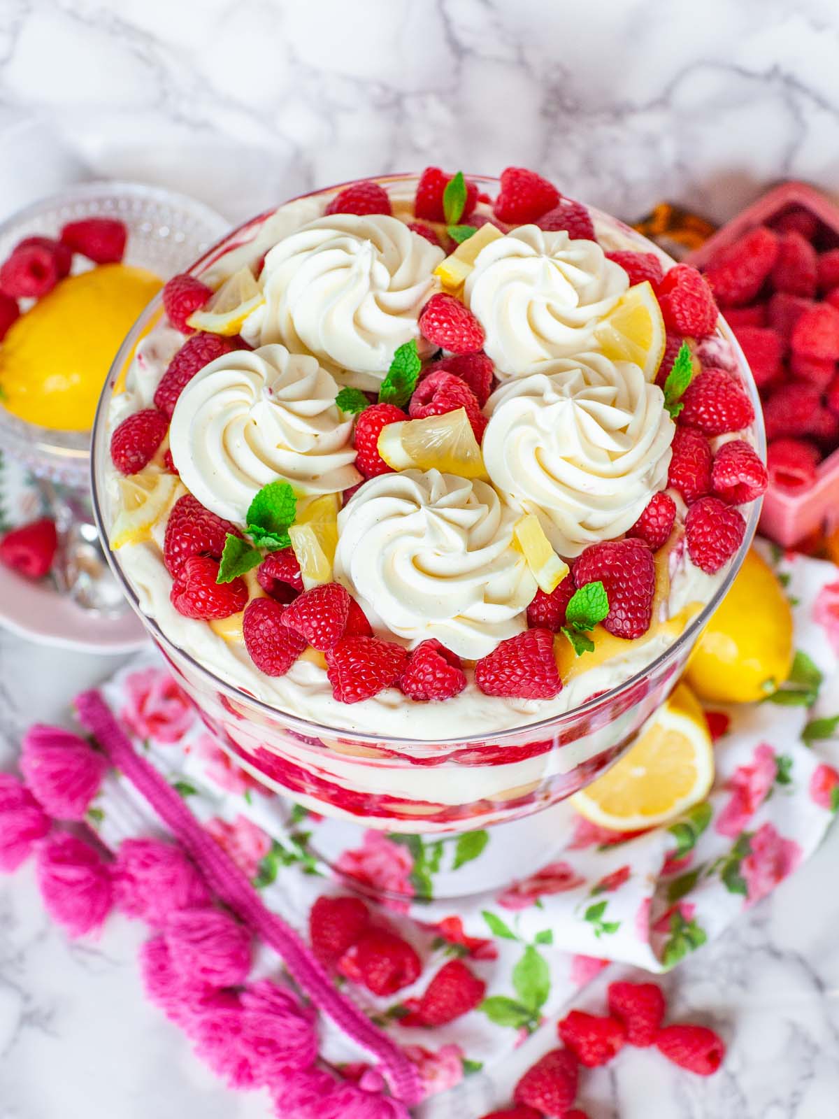 An overhead view of whipped cream dollops and raspberries on top of a dessert. On a table with lemons and raspberries.